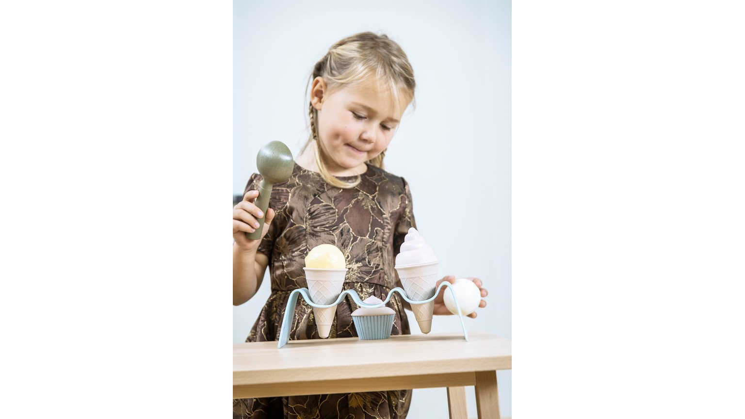 Person laver is med legetøjs-ismaskine og holder plastik-isterninger over små blå og grå beholdere.