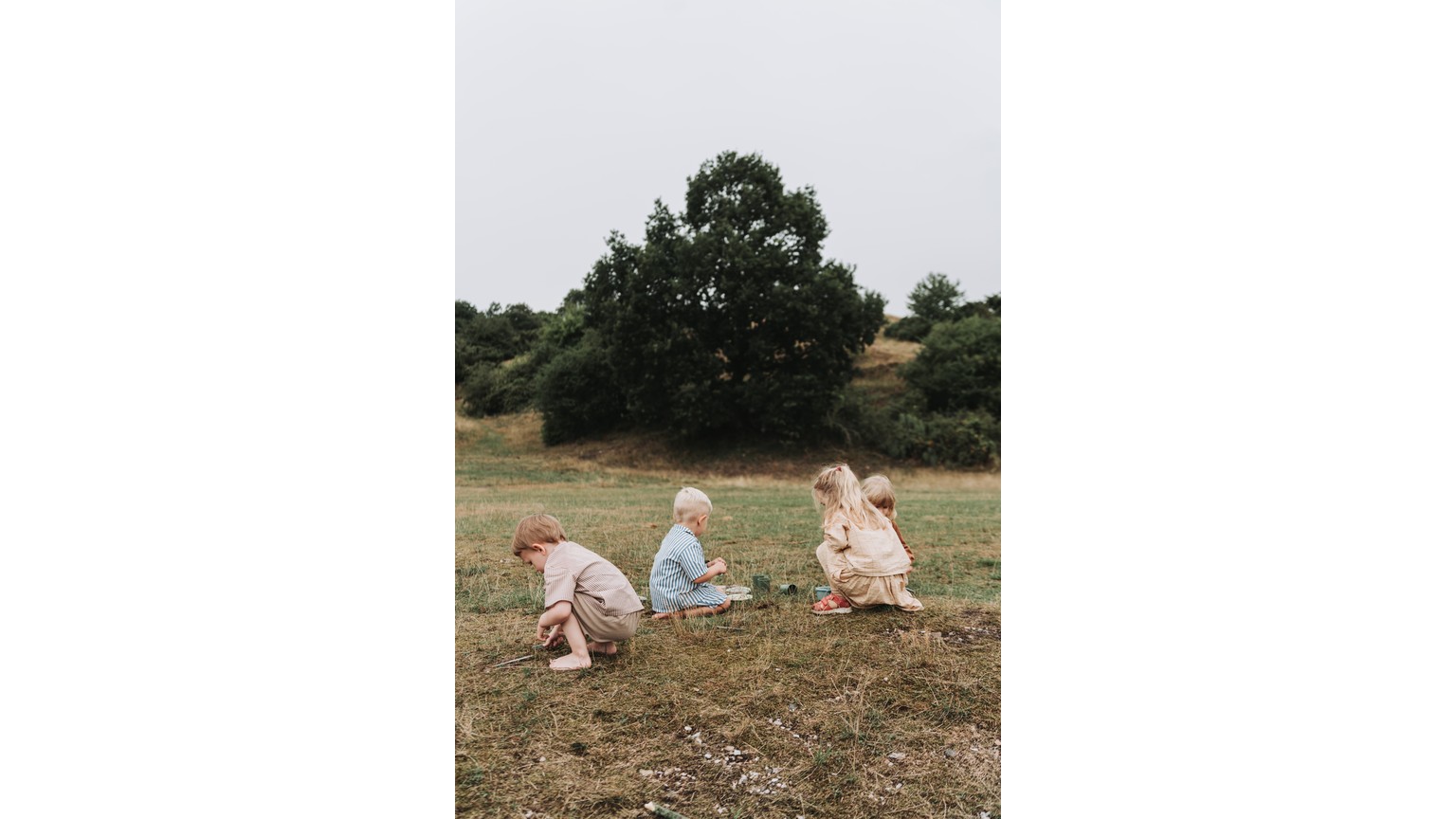 Små børn leger sammen på en bakke i naturen med træer i baggrunden.