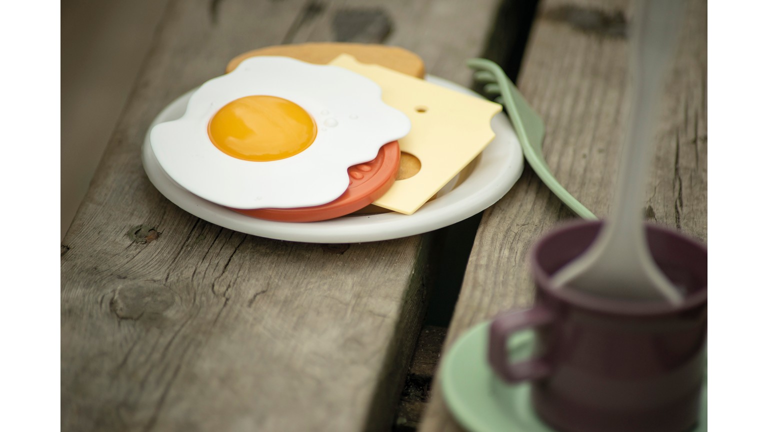 Spejlæg og pølse på en hvid tallerken på et træbord med en kop i baggrunden.
