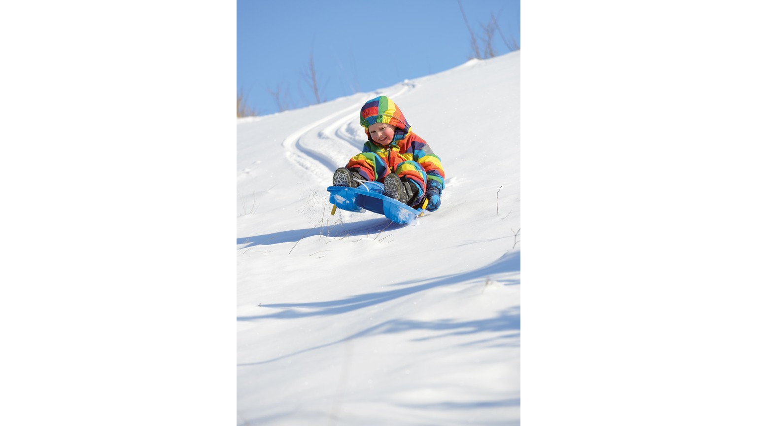 Person i farverig flyverdragt kører på blå kælk ned ad snedækket bakke