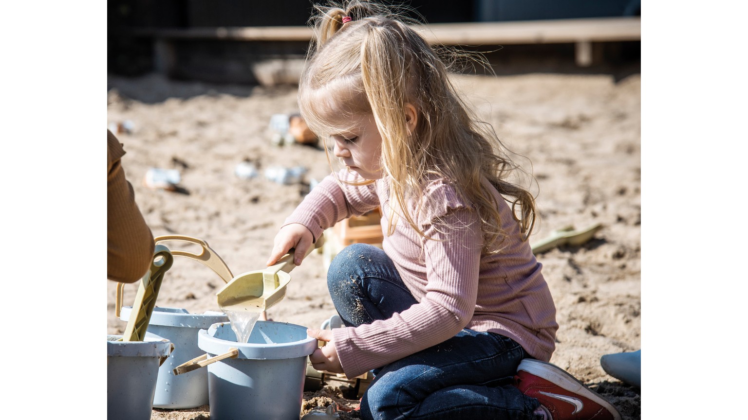Barn leger med sandlegetøj og spand ved sandkasse