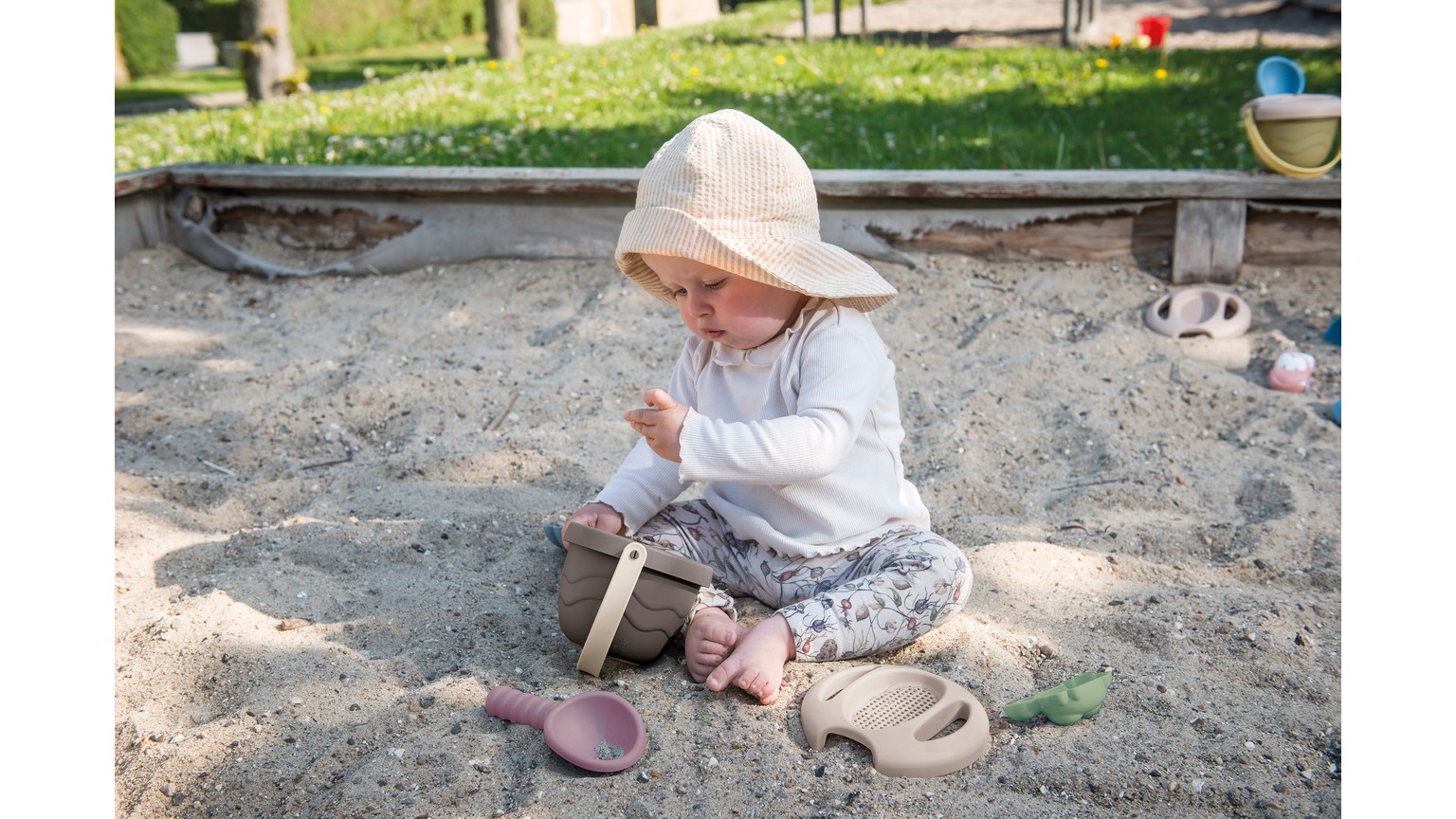 Barn leger i sandkasse med sandforme og skovl i lyse farver