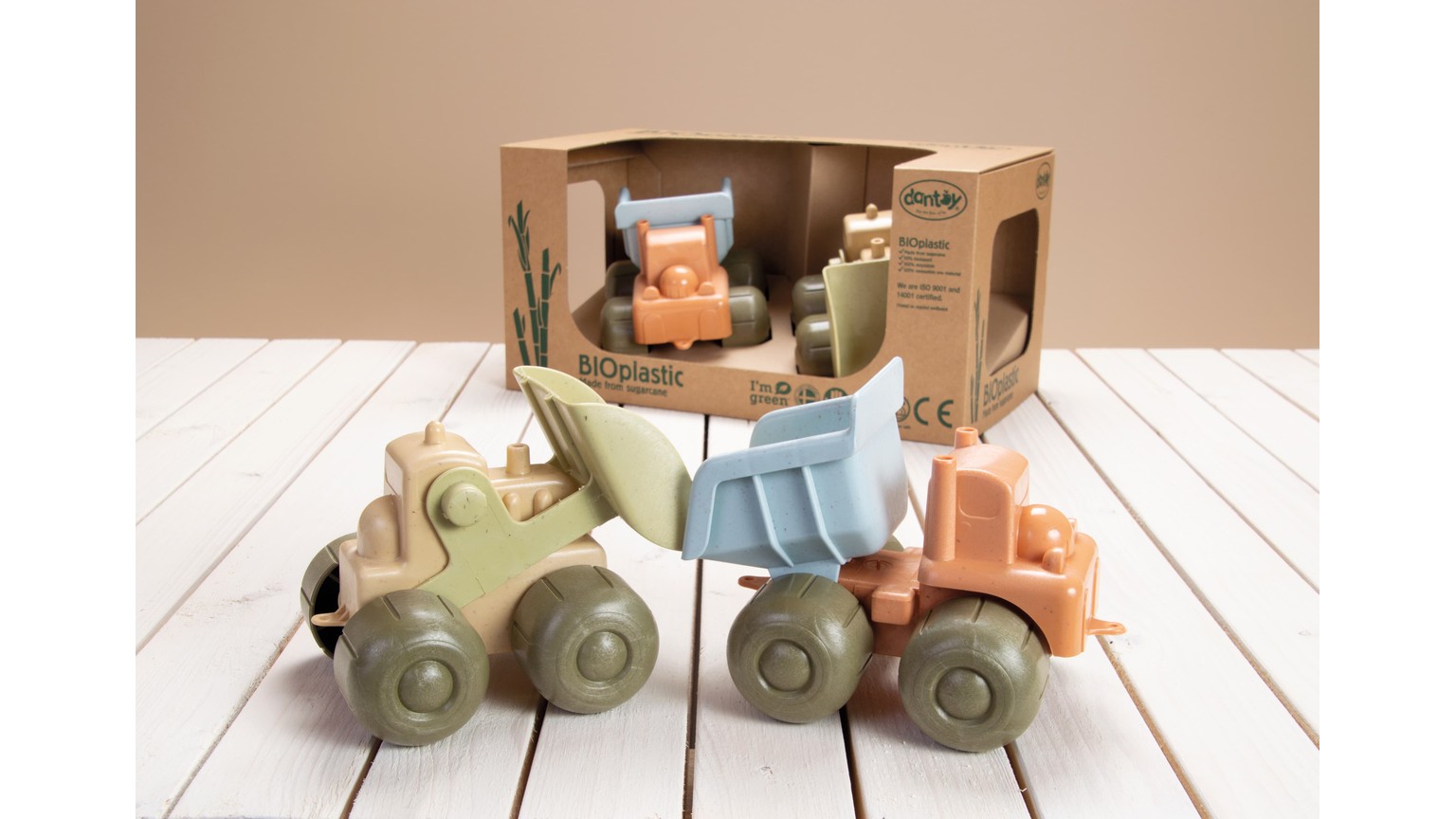 Tre bløde legetøjskøretøjer i pastelfarver - grøn, blå og orange - på et lyst trægulv