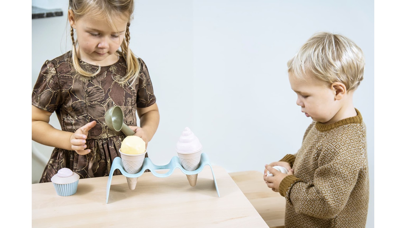 To børn sidder ved bord med lyserødt og blåt legetøjs-issæt og leger sammen