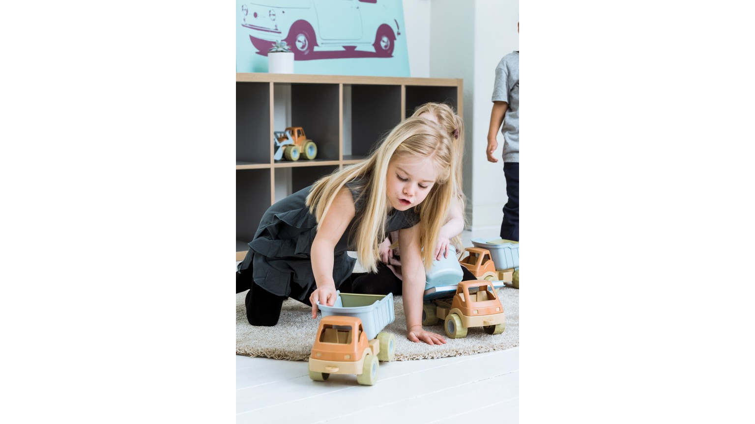 Barn leger med trælegetøjsbiler på gulvet ved en opbevaringshylde