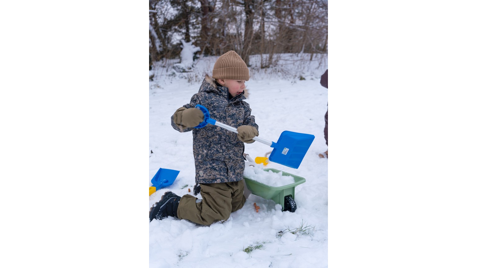 Barn leger med blåt og gult sandlegetøj i sneen på en vinterdag