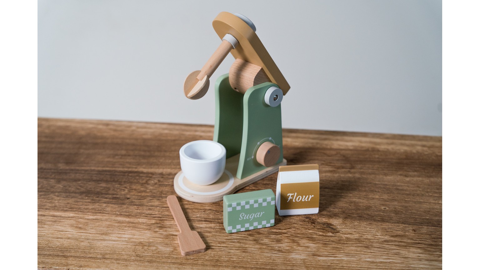 Grøn og hvid legeblender med tilbehør på træbord ved siden af papemballage.