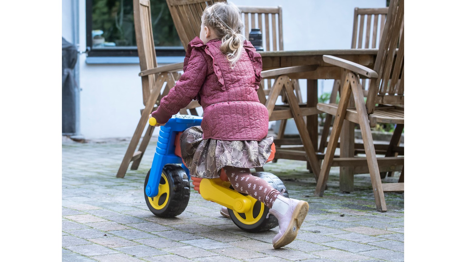Barn på gul og blå løbecykel på træterrasse ved havemøbler