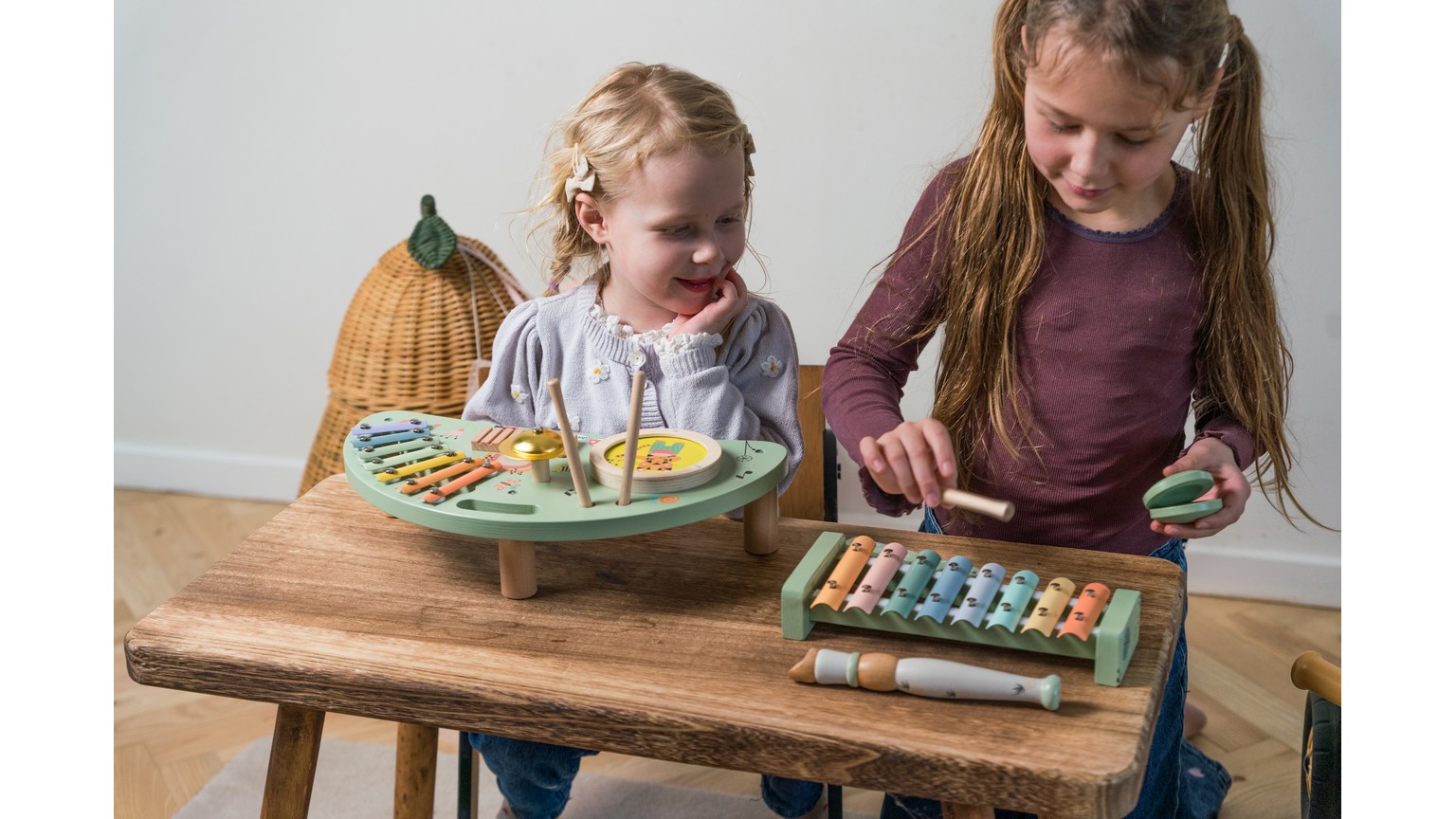 To børn ved træbord med musikinstrumenter - en med xylofon og en med tallerkner på farverige tallerkener.