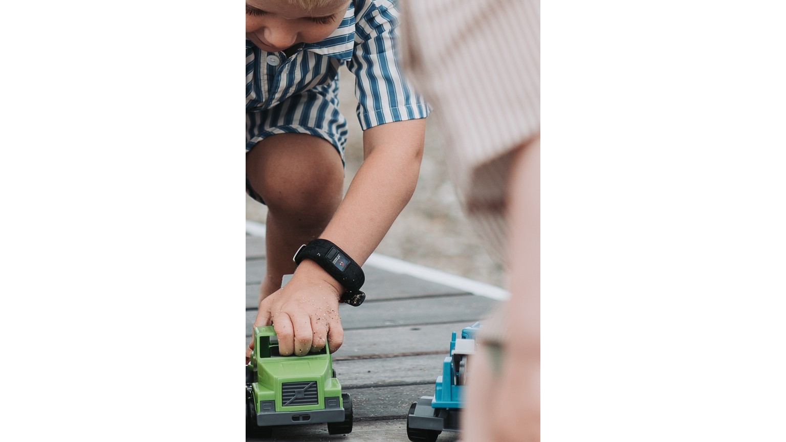 Et barn leger med grøn legebil på grå trappetrin, med blå legetøj ved siden af