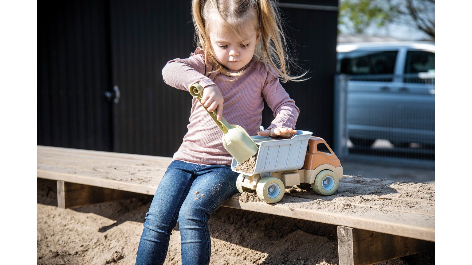 Barn leger med lille grå tipvogn på træbænk