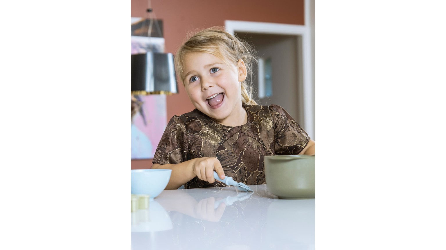 Glad barn ved køkkenbord med skål og kop under madlavning eller bagning