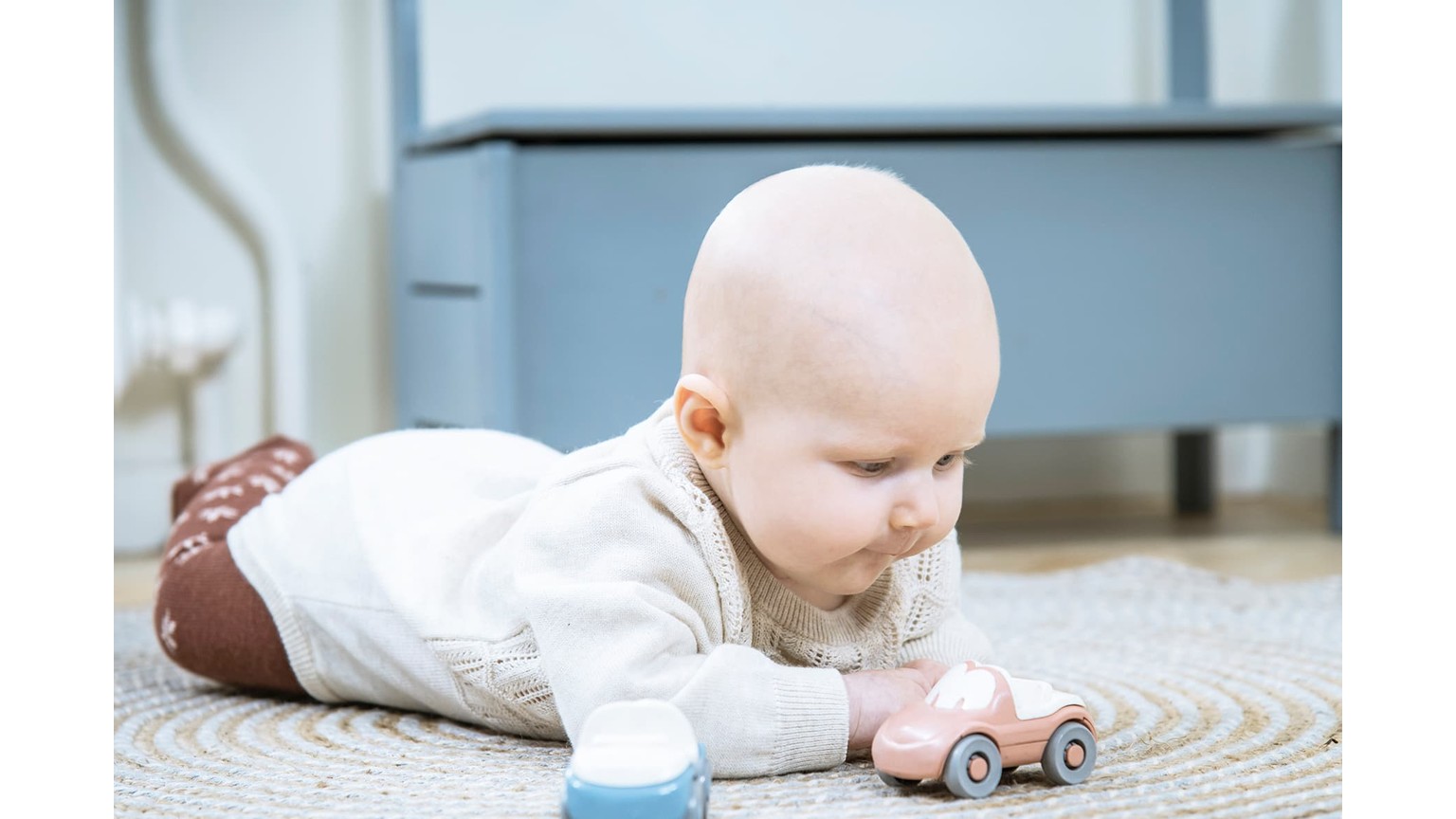 Baby på maven på gulv med lille lyserød legebil foran sig