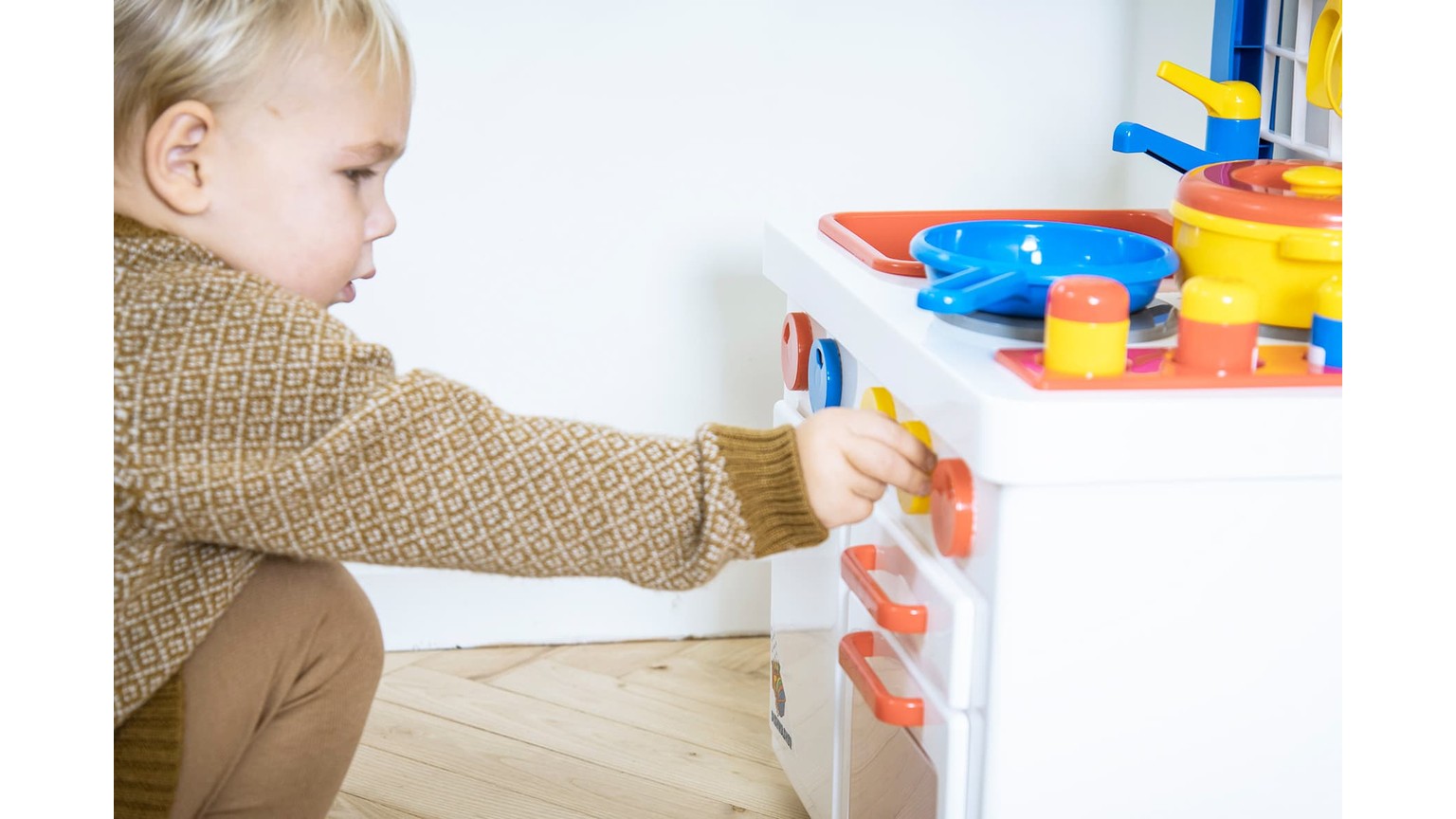Barn leger med farverigt legetøjskøkken i hvid med blå og røde detaljer