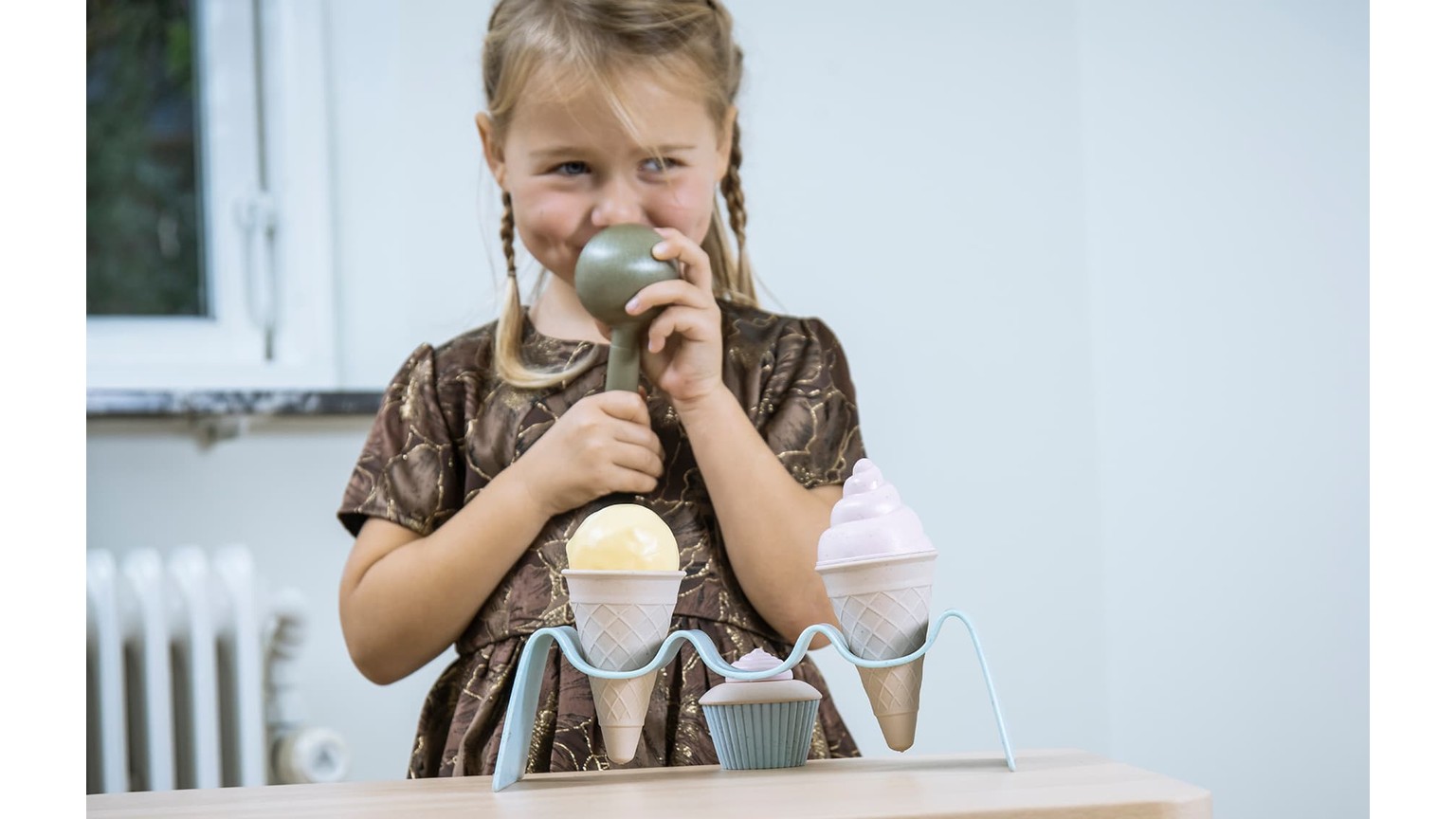 Barn med to lyserøde is-bægre ved hvidt bord ved vindue