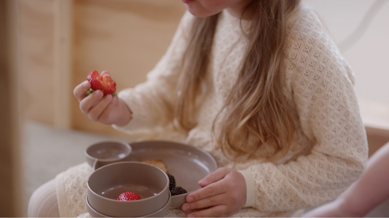 Person i hvid sweater holder jordbær over skåle i mørke nuancer