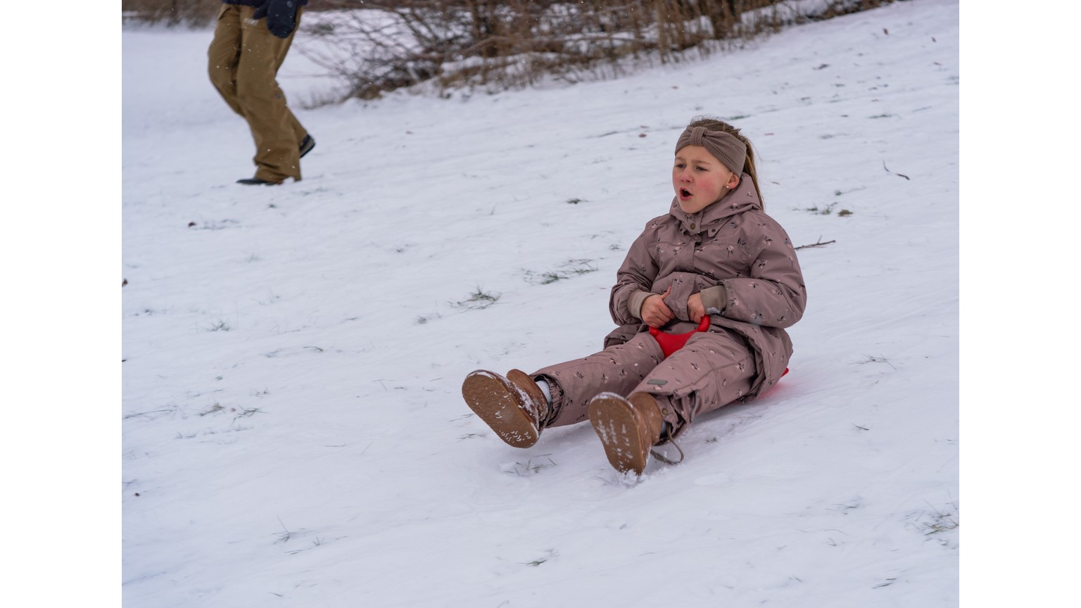 Barn på kælketur i sneen med rød plastikslæde