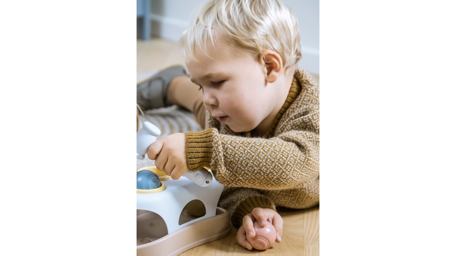 Lille barn i brun trøje leger med hvidt hammerbræt på bord